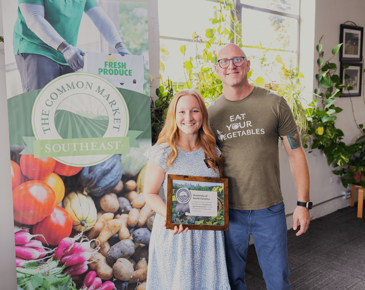 A member of Carolina Food Co. from the University of South Carolina holds the Common Market Farmer's Champion Award next to a representative from The Common Market.